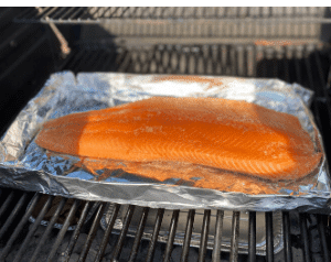Salmon on aluminum foil smoking on a grill.