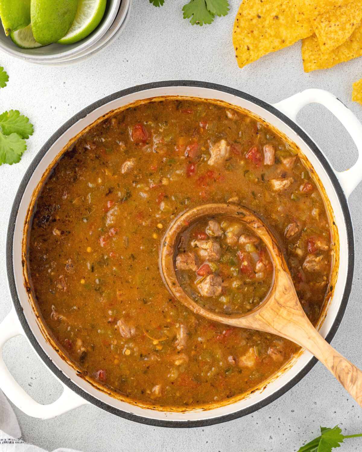 A wooden ladle is scooping chile verde from the Dutch oven.