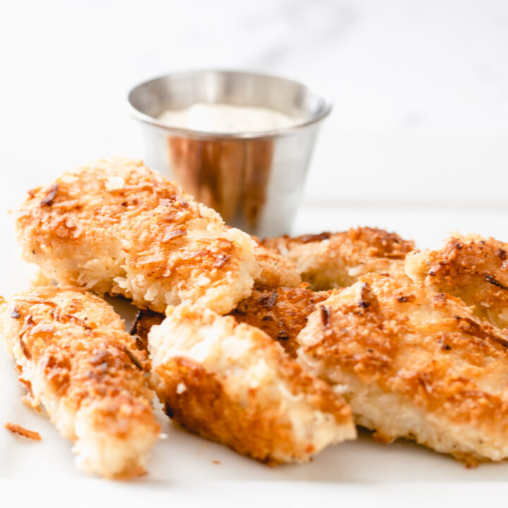 Close up view of coconut chicken strips on a plate with a ramekin of ranch dressing.