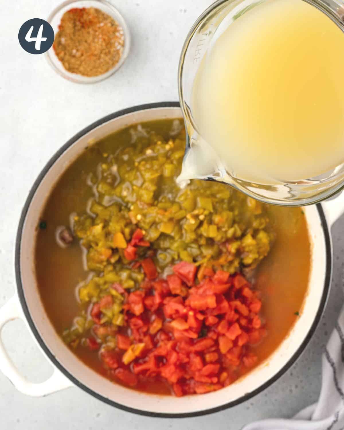 Pouring chicken broth from a measuring cup into a pan with green chiles and diced tomatoes.