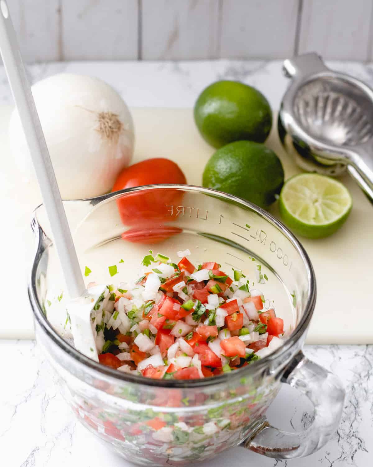 Bowl of pico de gallo with onion, tomato, and limes on a cutting board in the background.