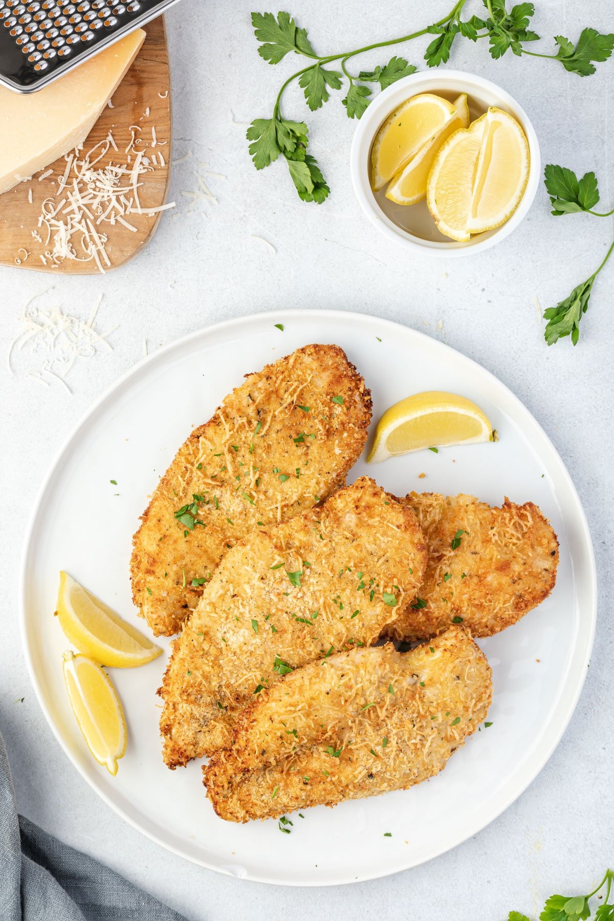 Breaded chicken cutlets on a plate with lemon wedges and parmesan.