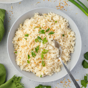 Bowl of jasmine rice made with coconut milk, topped with green onions and toasted coconut.