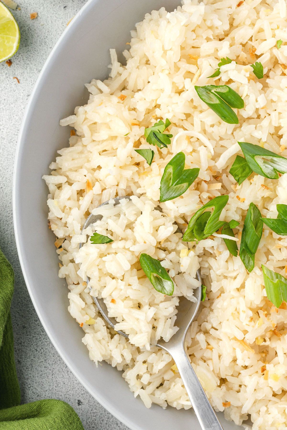 Close up of the left half of a bowl of jasmine coconut rice, topped with green onions and toasted coconut.