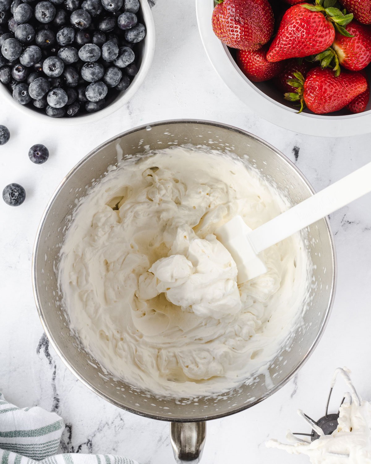 Whipped cream in a bowl, with smaller bowls of blueberries and strawberries at the top of the photo.