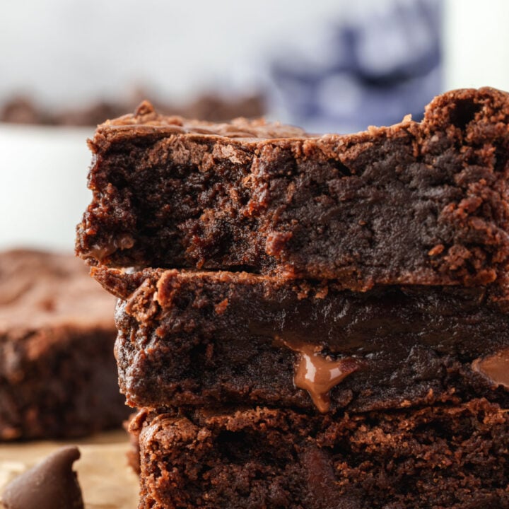 A stack of 3 gooey fudge brownies with melty chocolate pieces and a bite out of the top one.