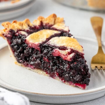 A slice of huckleberry pie with a lattice crust on a plate, with a gold fork.