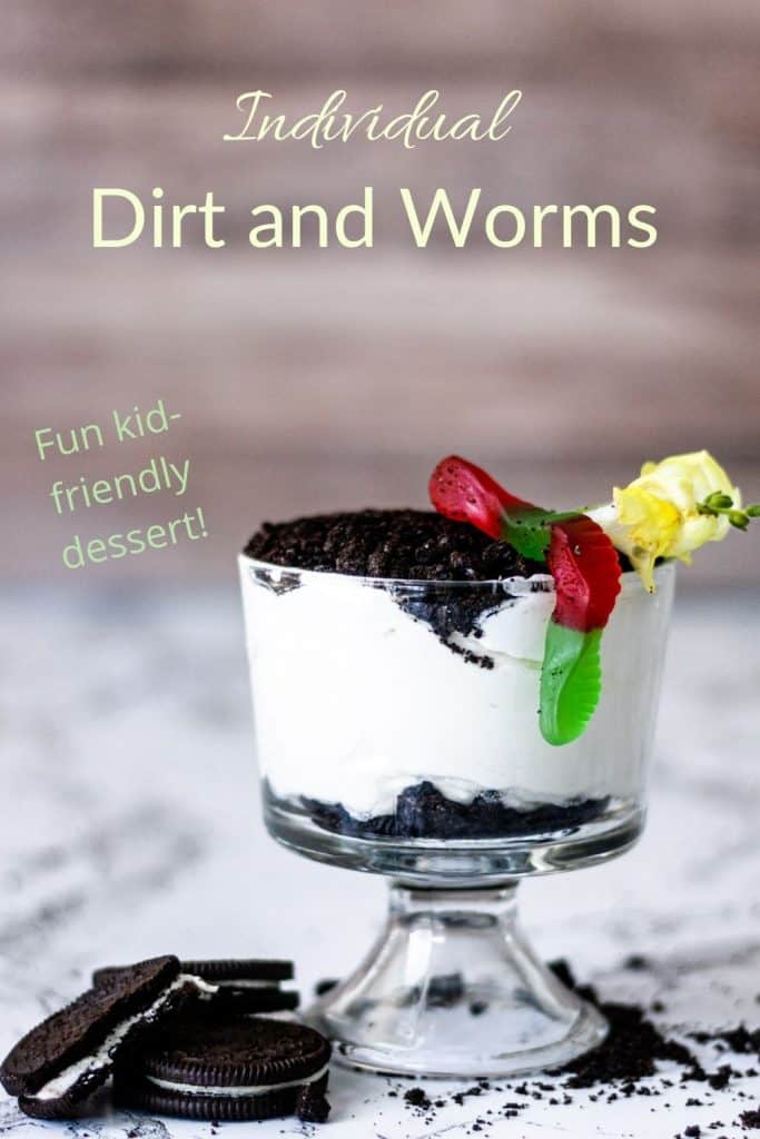 Individual container of dirt cake with gummy worm on top and Oreo crumbles on the counter.