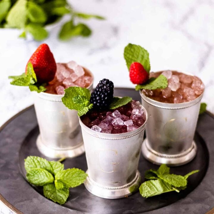 3 cups of berry mint juleps on a tray, with mint in the background.