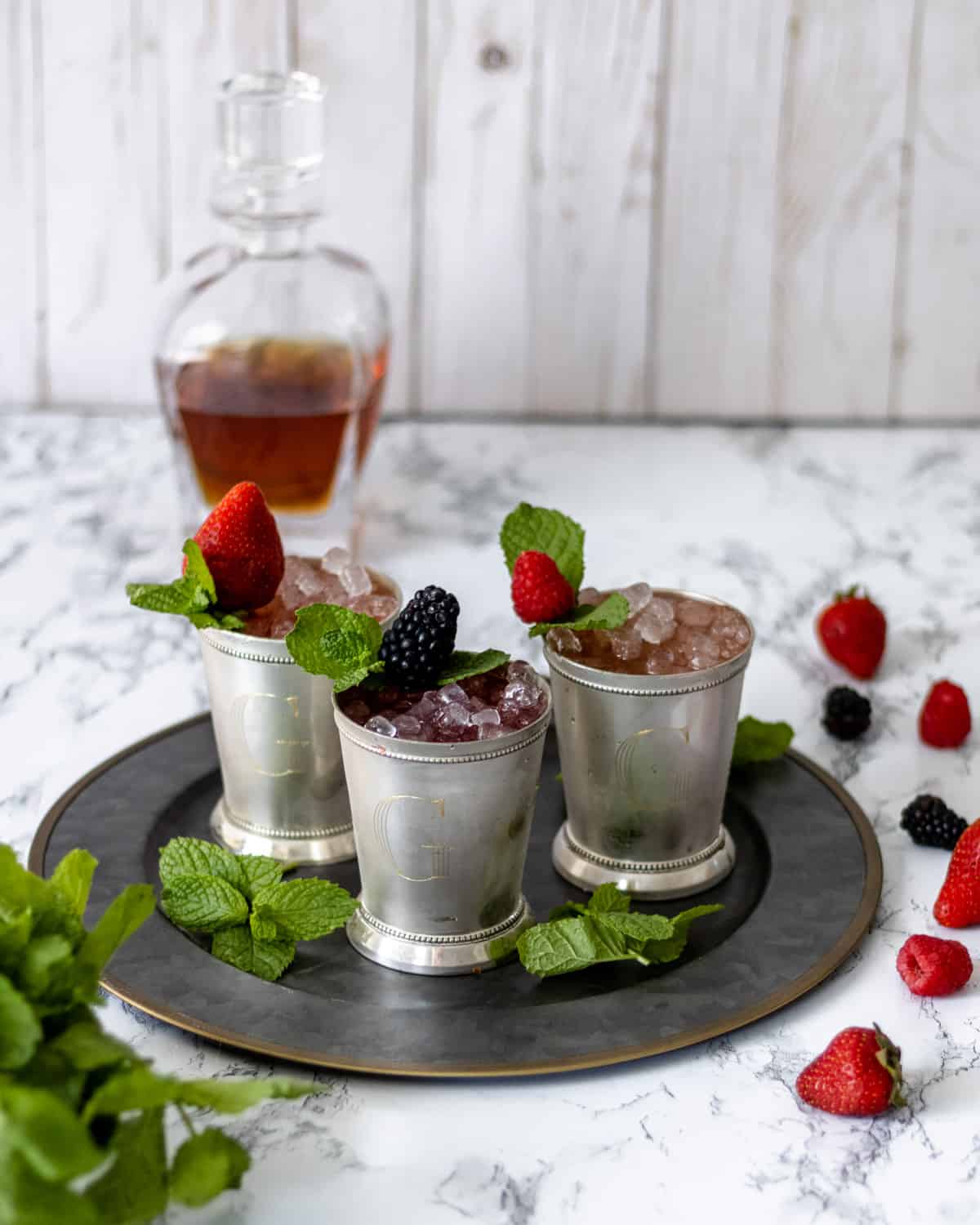 3 berry mint juleps with berries and mint scattered around.