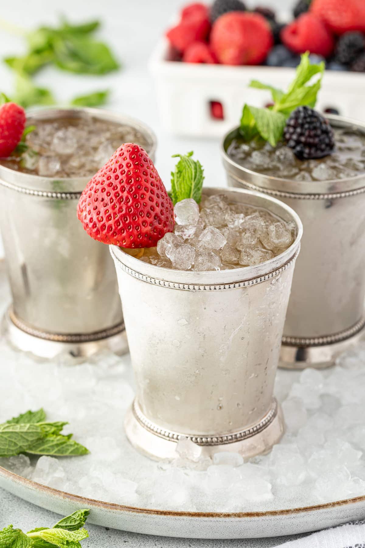 Three silver cups filled with crushed ice, berries, and mint, with more berries in the background.