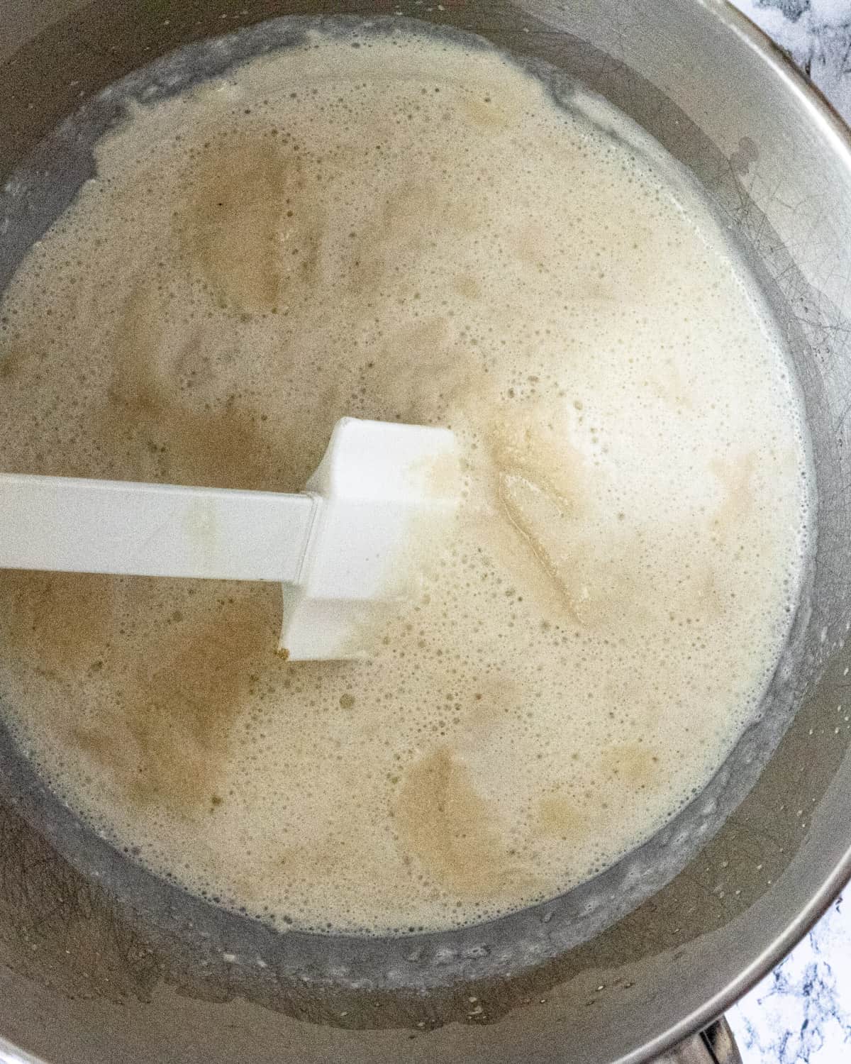 Beige liquid is bubbling in a metal bowl.