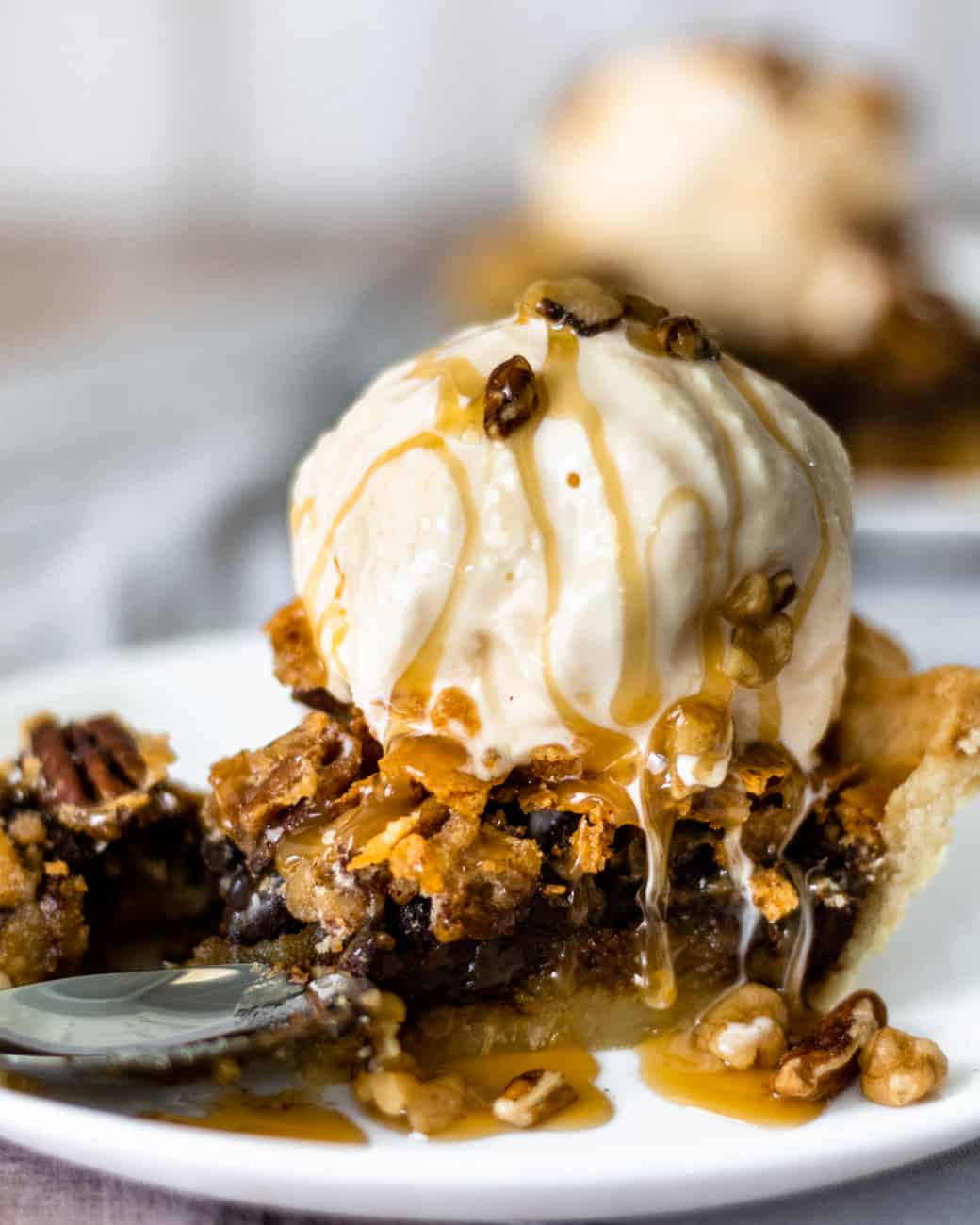 slice of chocolate walnut pecan pie with ice cream on top and caramel drizzled all over.
