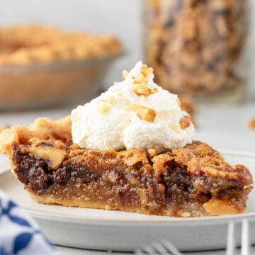 Chocolate walnut pie on a plate, with whipped cream on top and walnuts sprinkled on the cream.