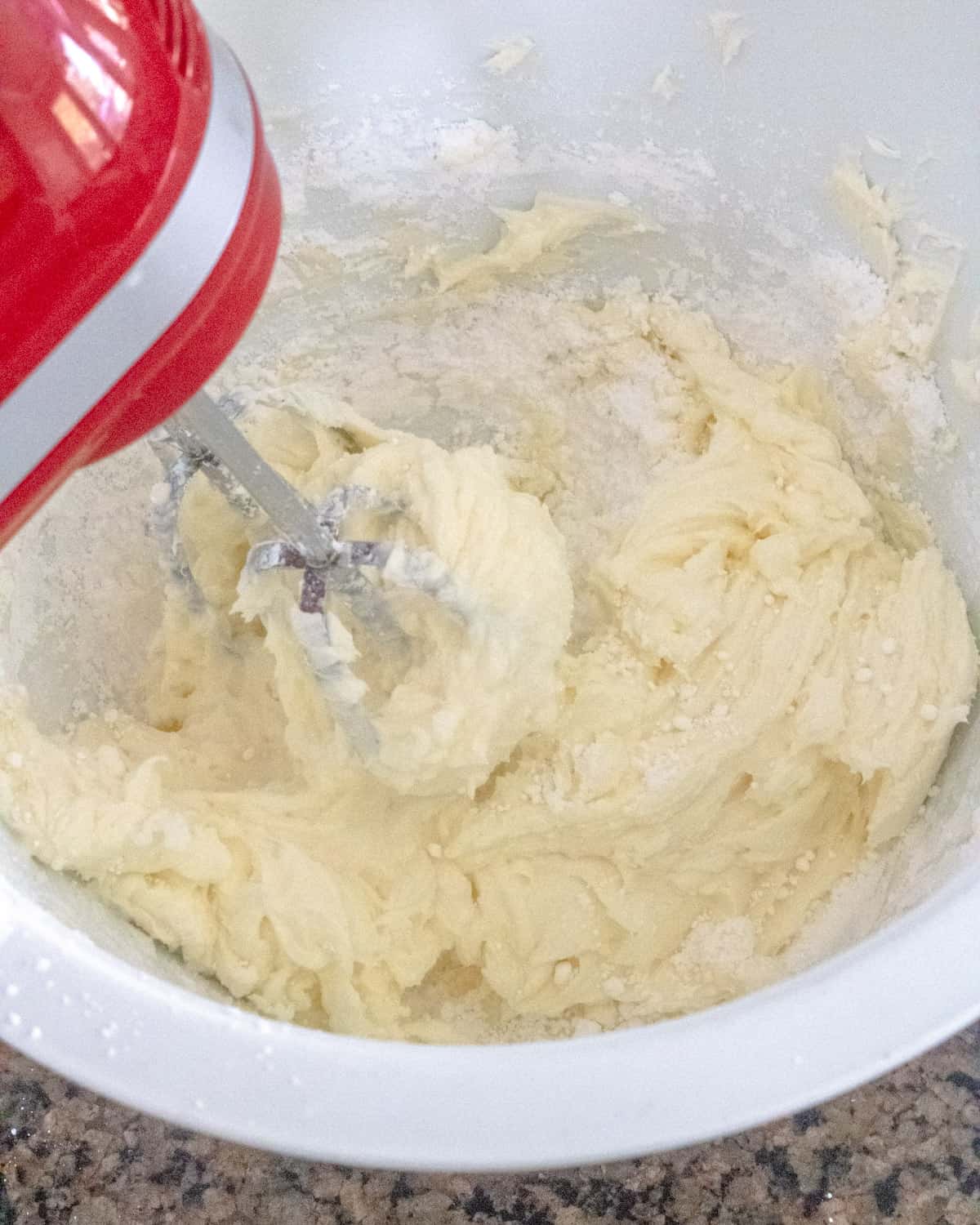 Bowl of cream cheese and powdered sugar mixed together with a red hand mixer.