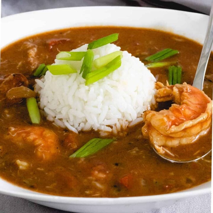 Bowl of louisiana gumbo with a ball of rice in the middle. Spoon is scooping up a piece of shrimp.