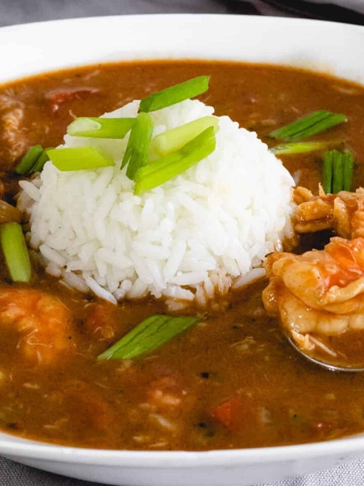 Bowl of louisiana gumbo with a ball of rice in the middle. Spoon is scooping up a piece of shrimp.