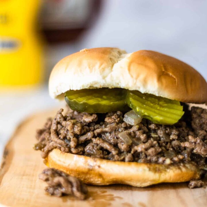 Loose meat sandwich with 2 pickles, condiments in background