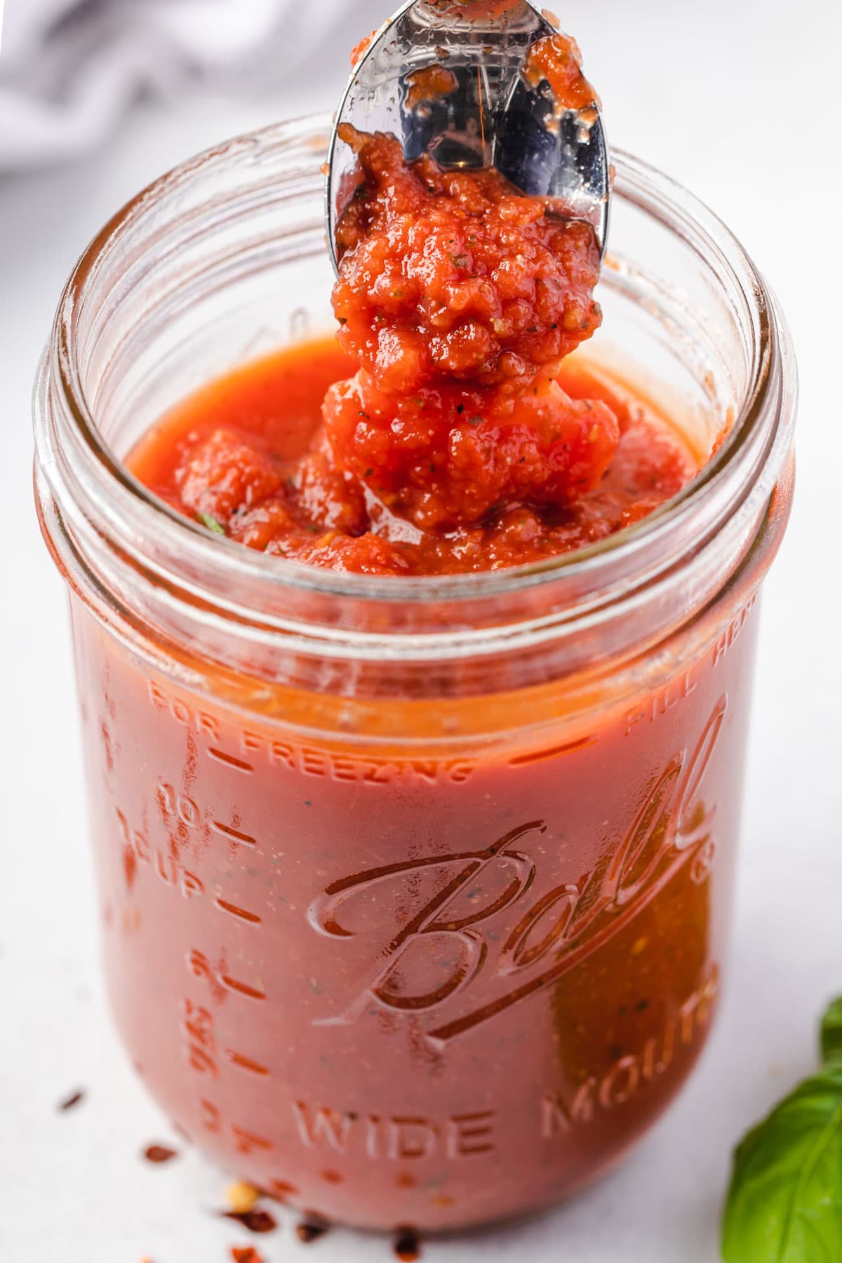 Jar of marinara sauce with a spoon straight up and sauce dripping off of spoon.