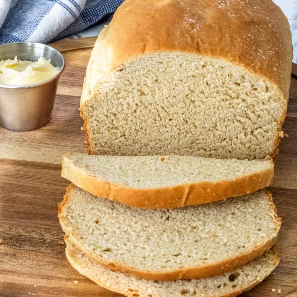 Honey wheat bread with 3 slices laying forward. Ramekin of butter next to it.