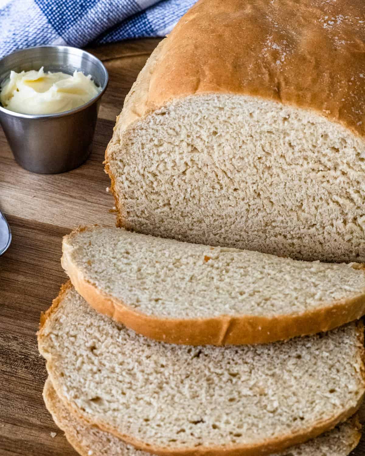 Loaf of bread with 3 slices, and a ramekan of butter on the side.