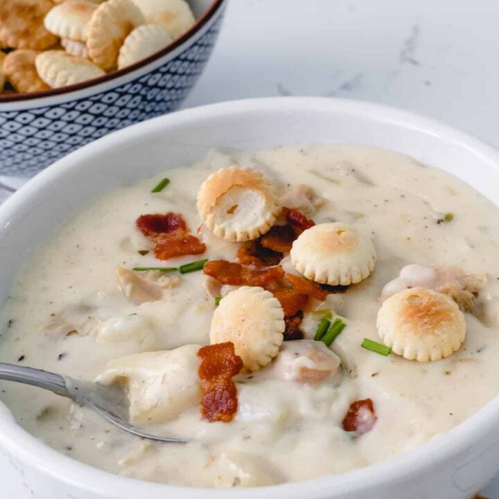 Bowl of clam chowder, topped with bacon pieces and oyster crackers.