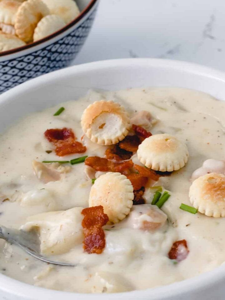 Bowl of clam chowder, topped with bacon pieces and oyster crackers.