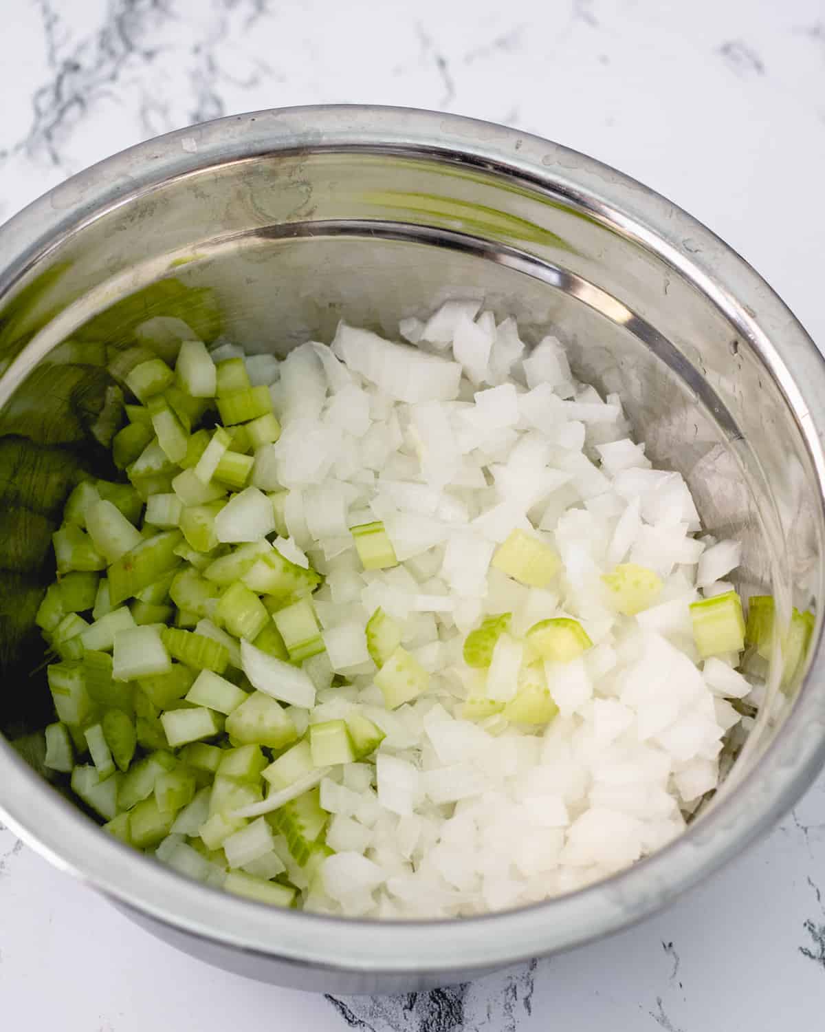 Chopped onions and celery in a stainless bowl.