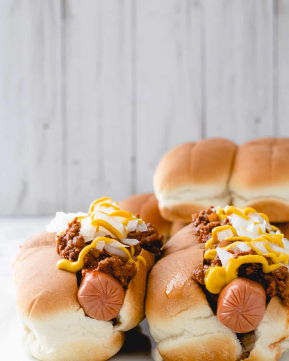 Two coney dogs with a pile of buns behind them.