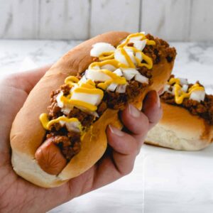 A person holding a coney dog.