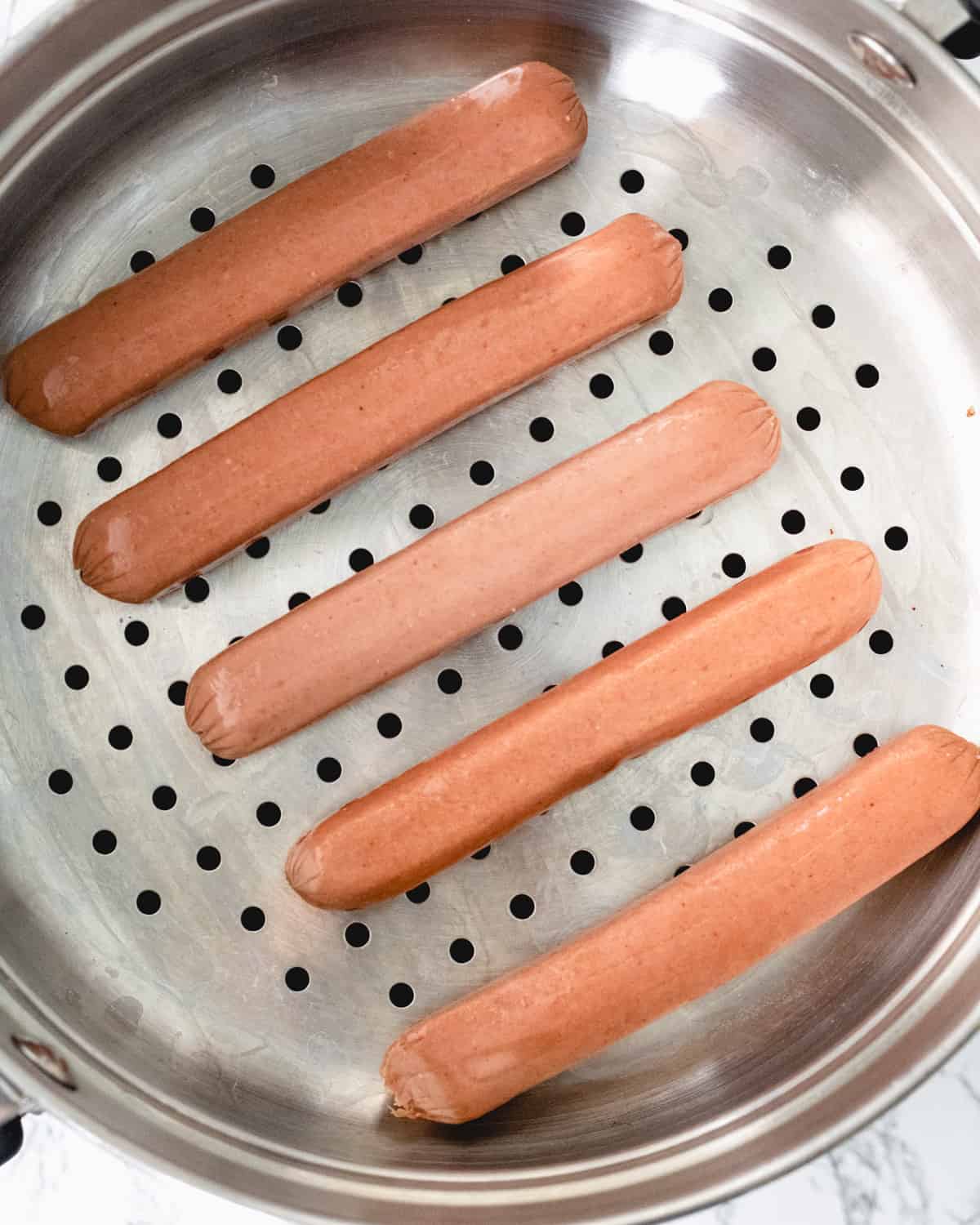 Five hot dogs laying in a steamer basket.