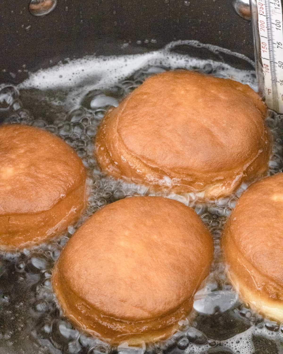 4 donuts fried in hot oil. They are medium-brown on top.