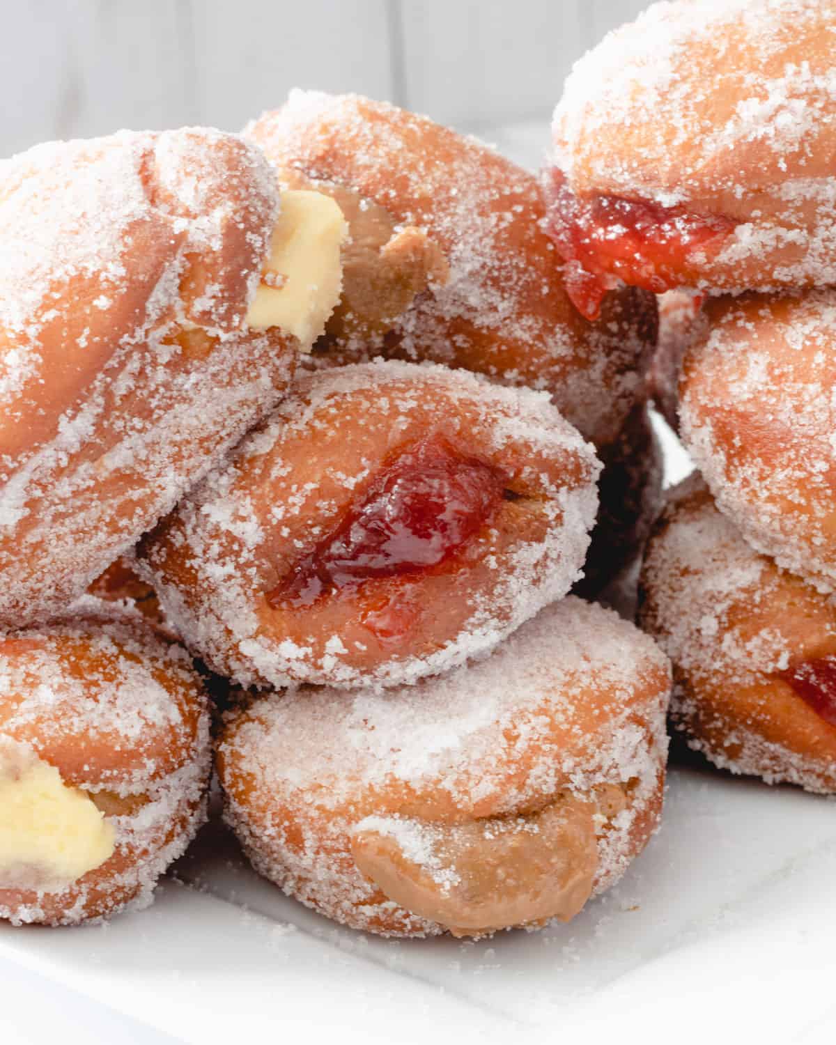 Paczki donuts piled on a plate. There are different fillings in them, including custard, strawberry, and dulce de leche.