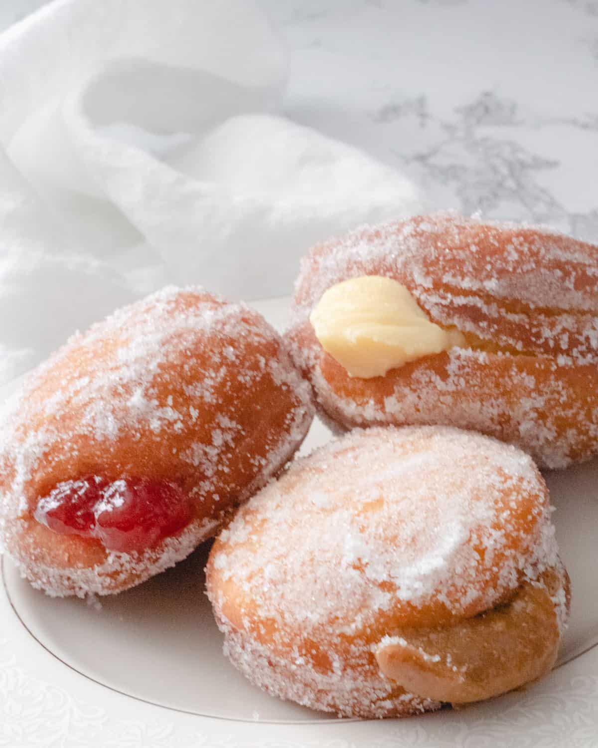 Three paczkis on a plate with strawberry jam, custard, and dulce de leche filling.