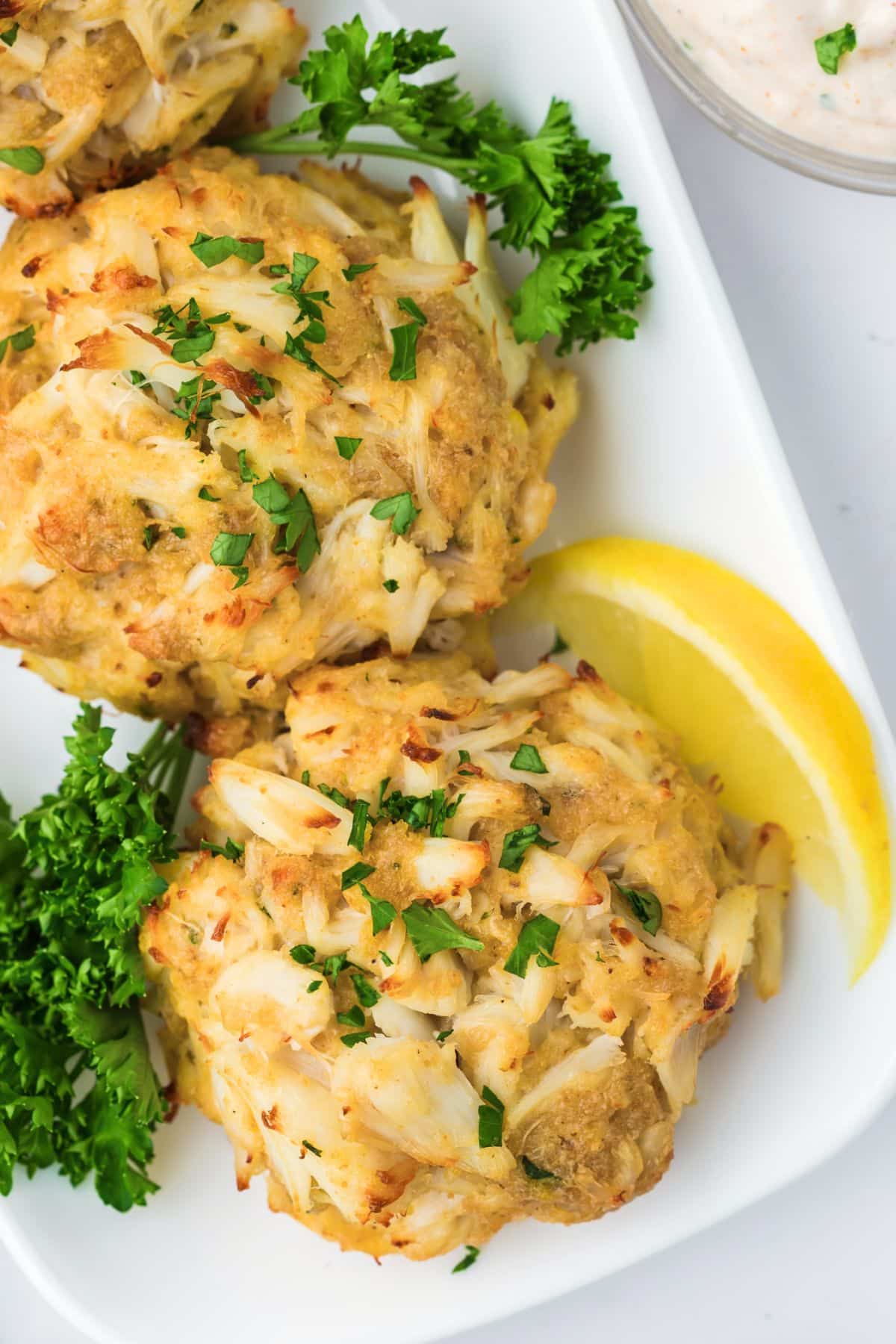 2 crab cakes on a platter with lemon wedges.