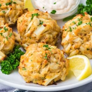 A platter of baked crab cakes with a bowl of sauce.