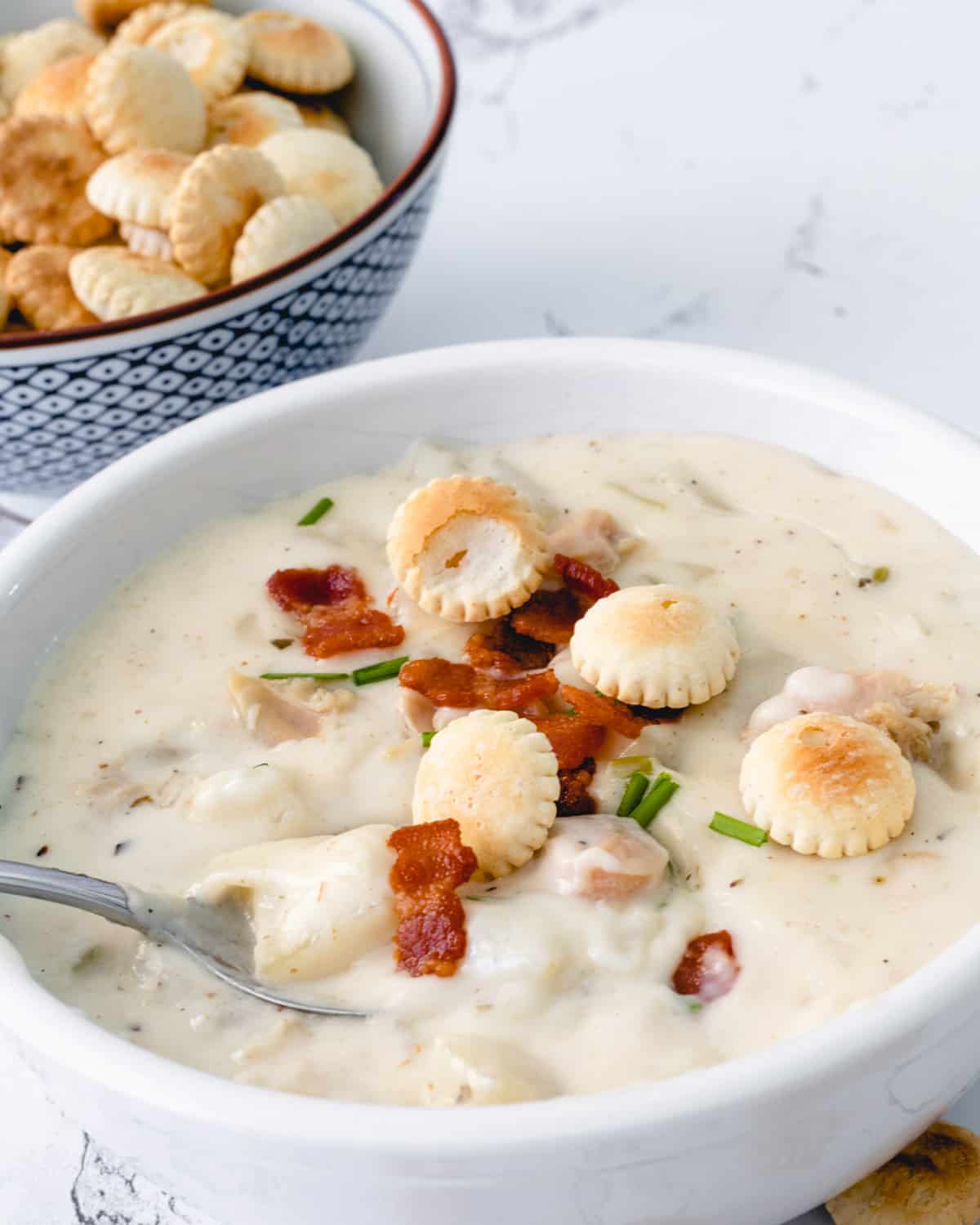 Bowl of Boston Clam Chowder with all of the toppings. A spoon dipped into the bowl.