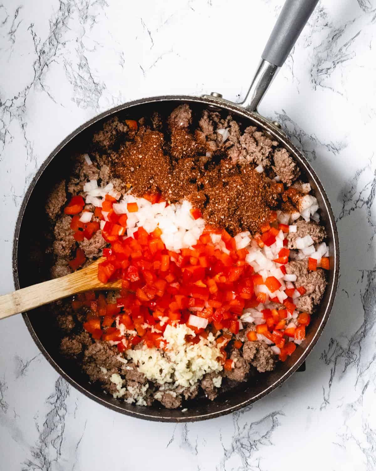 Onions, red bell pepper, garlic, and seasonings are added to the pan of ground beef.