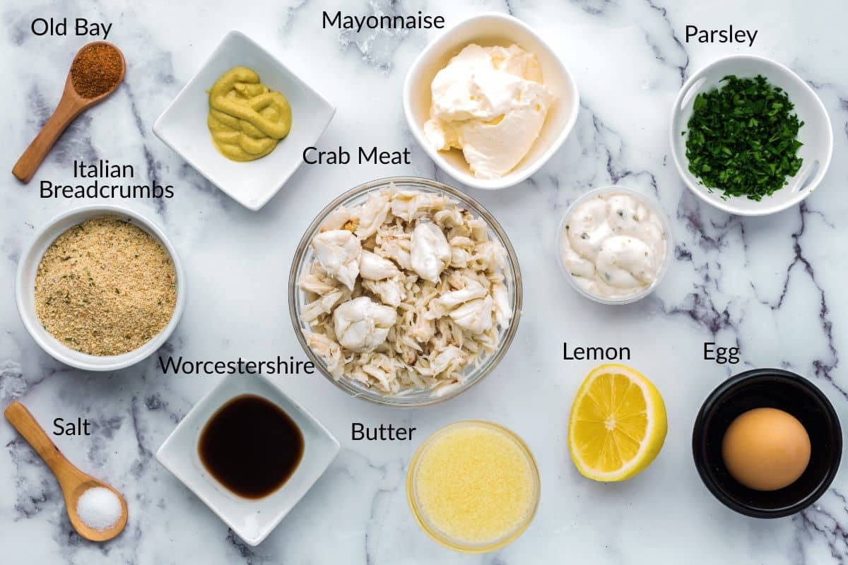 Bowls of crab cake ingredients including crab meat, egg, mayonnaise, parsley, lemon, butter, and seasonings.