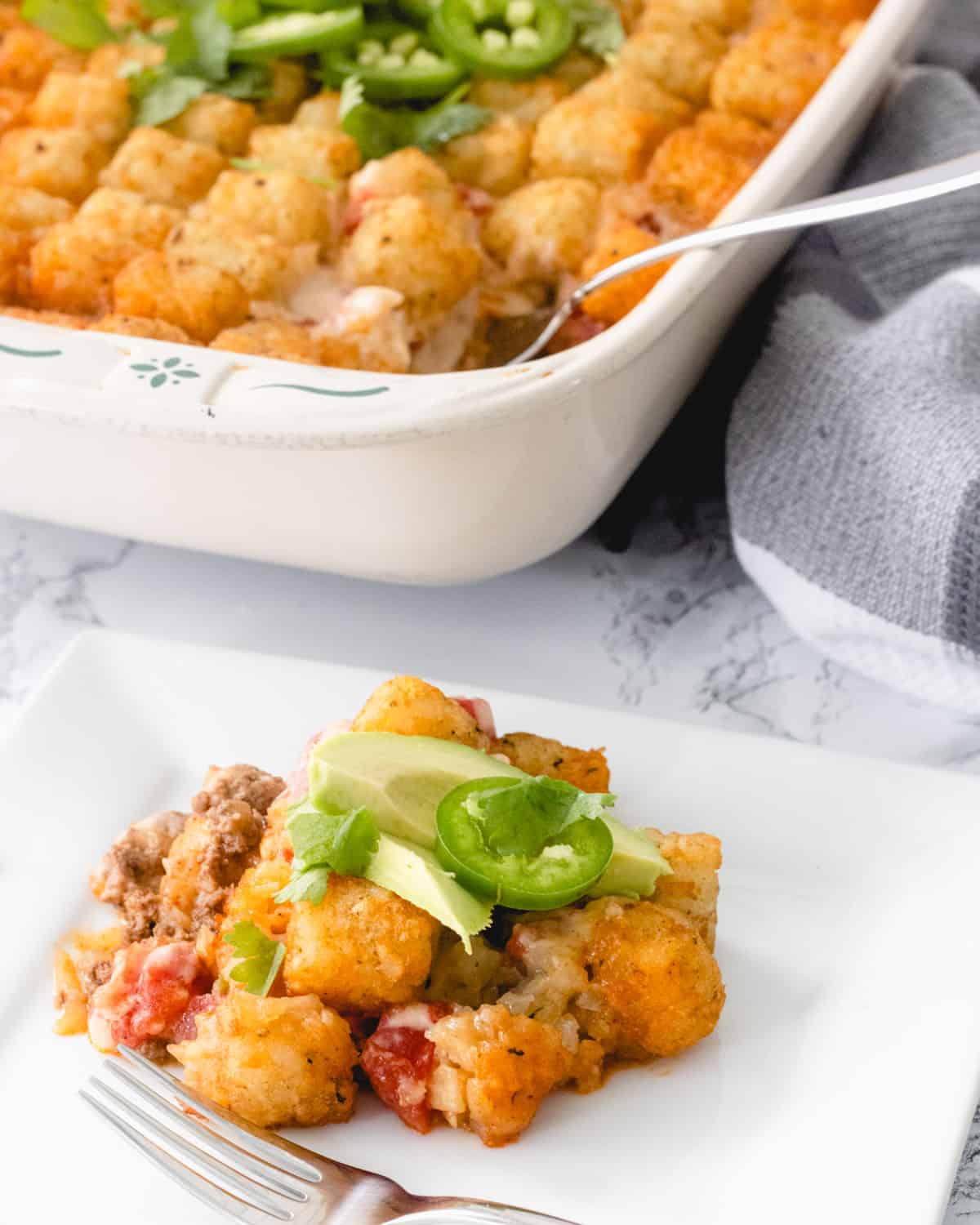 Taco casserole with tater tots, served on a plate with avocado, jalapeno, and cilantro.