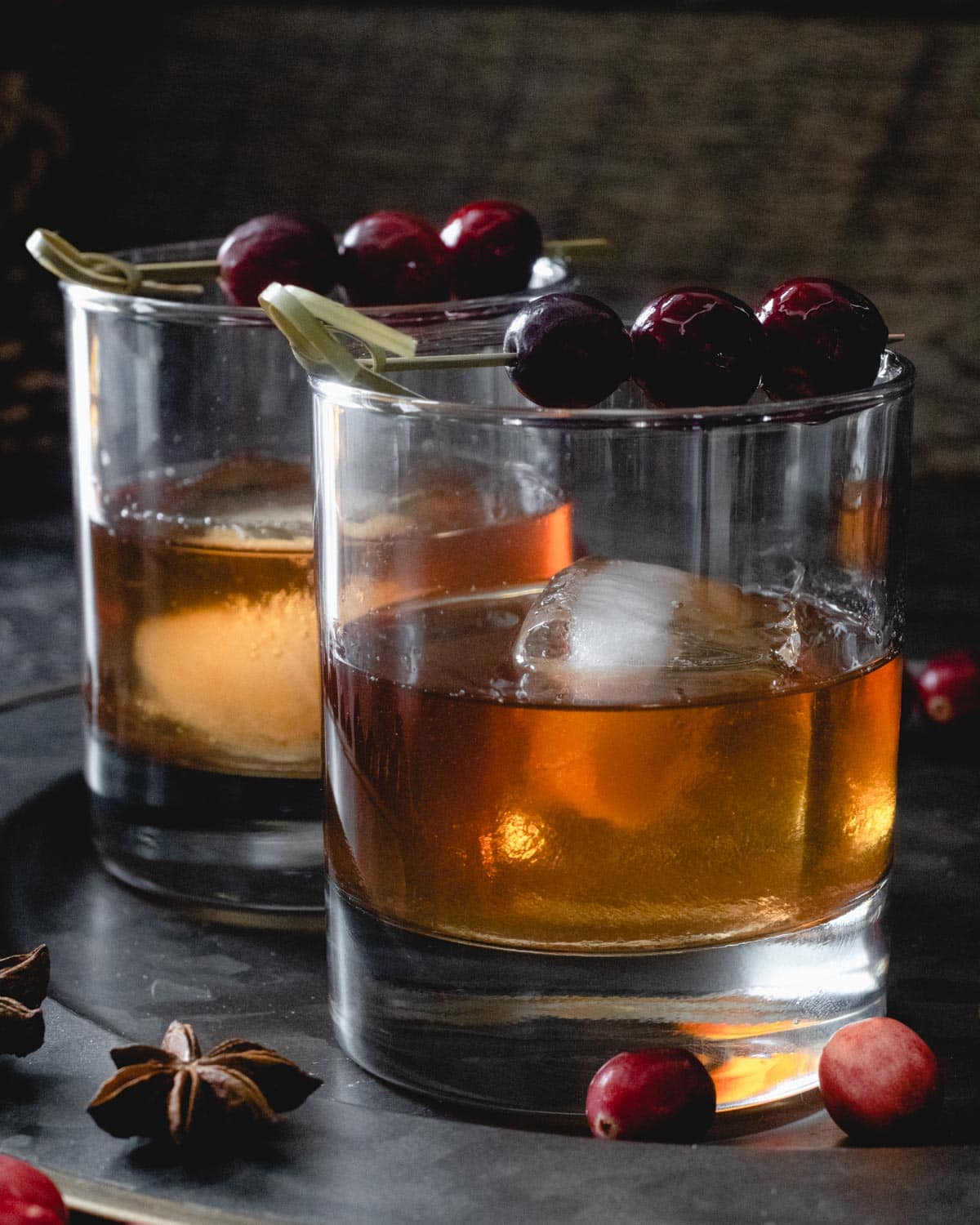 Two cranberry old fashioned cocktails in rocks glasses, garnished with cranberries.