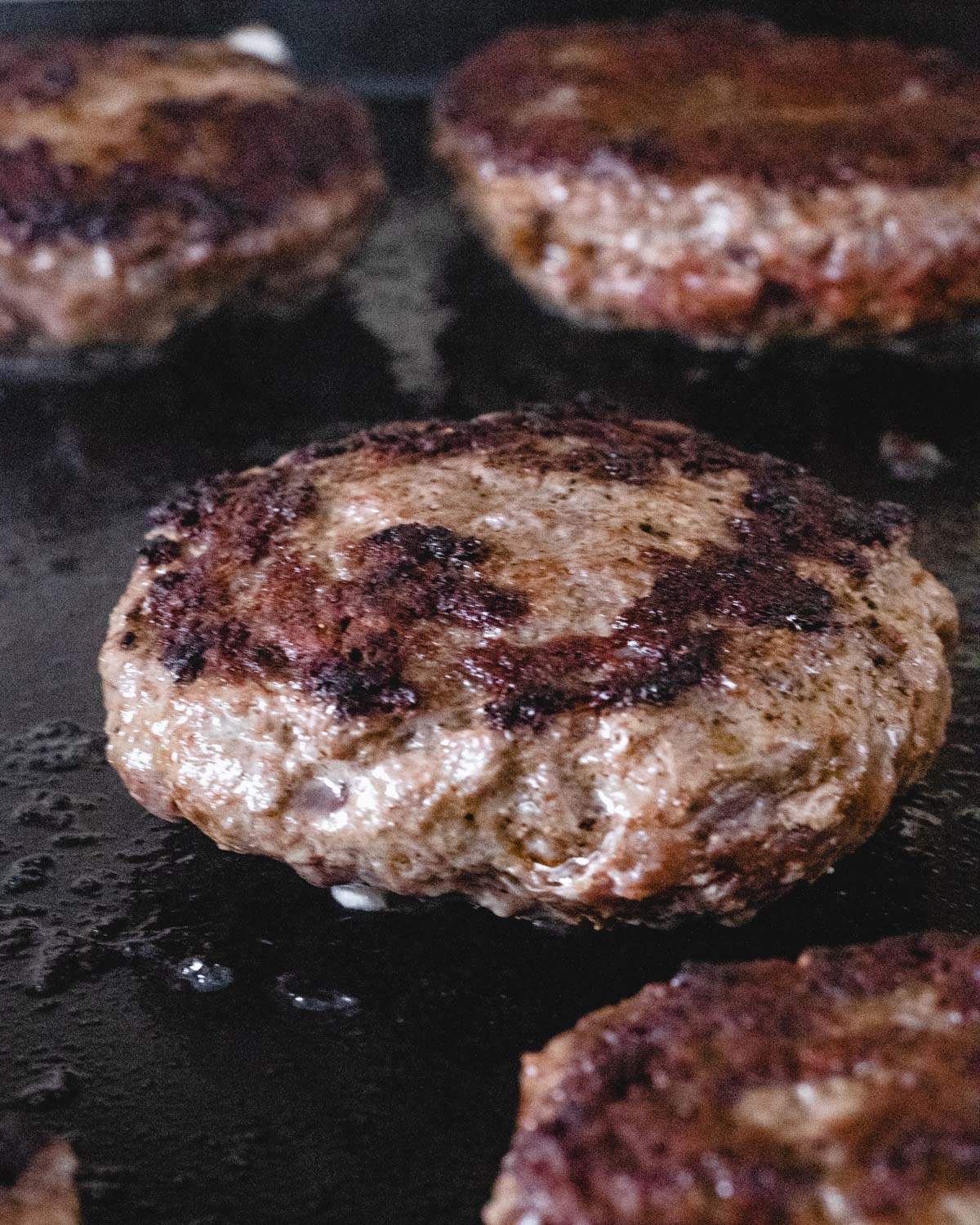 4 elk patties on a grill.