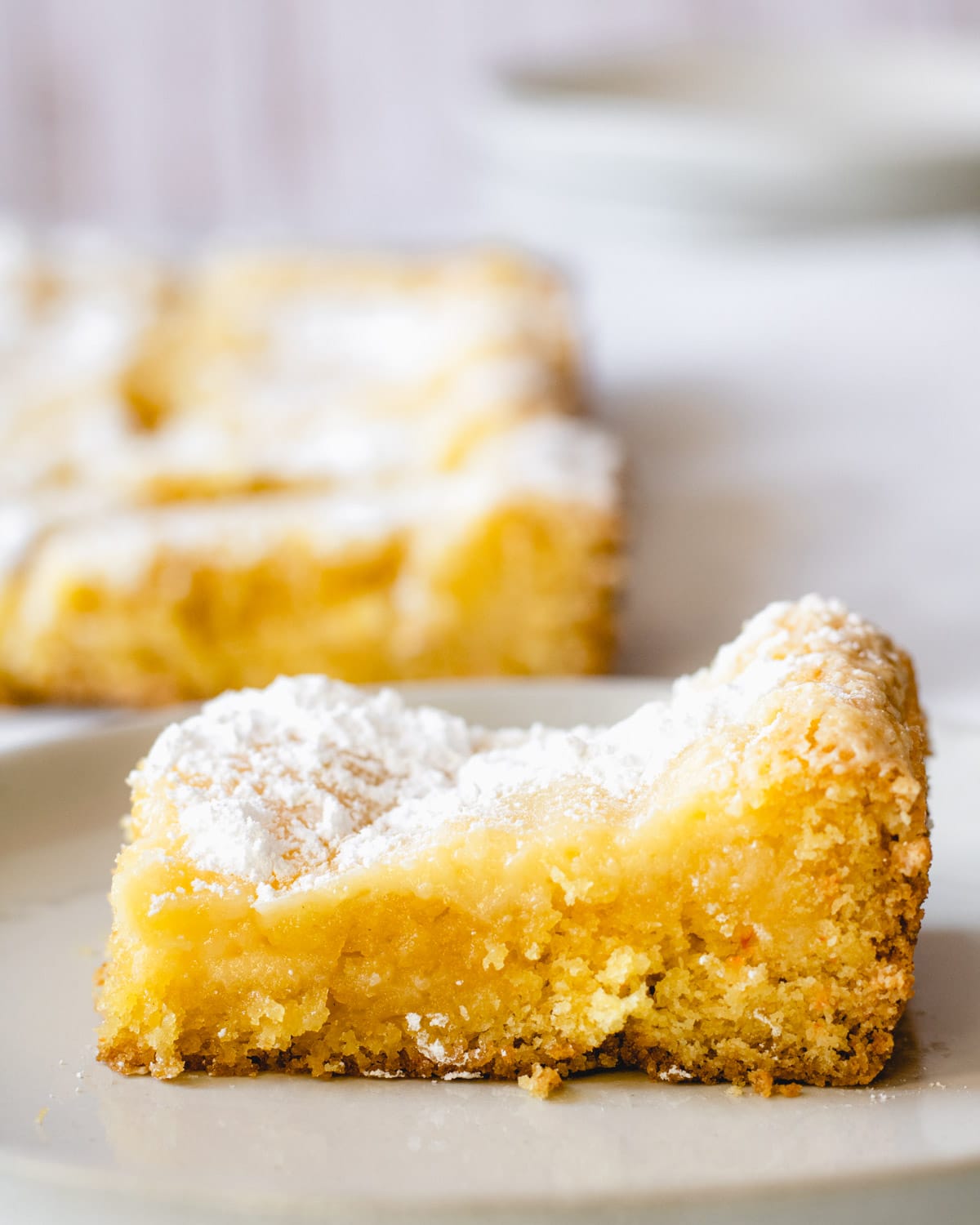 One square of gooey butter cake on a plate with the remaining cake in the background,
