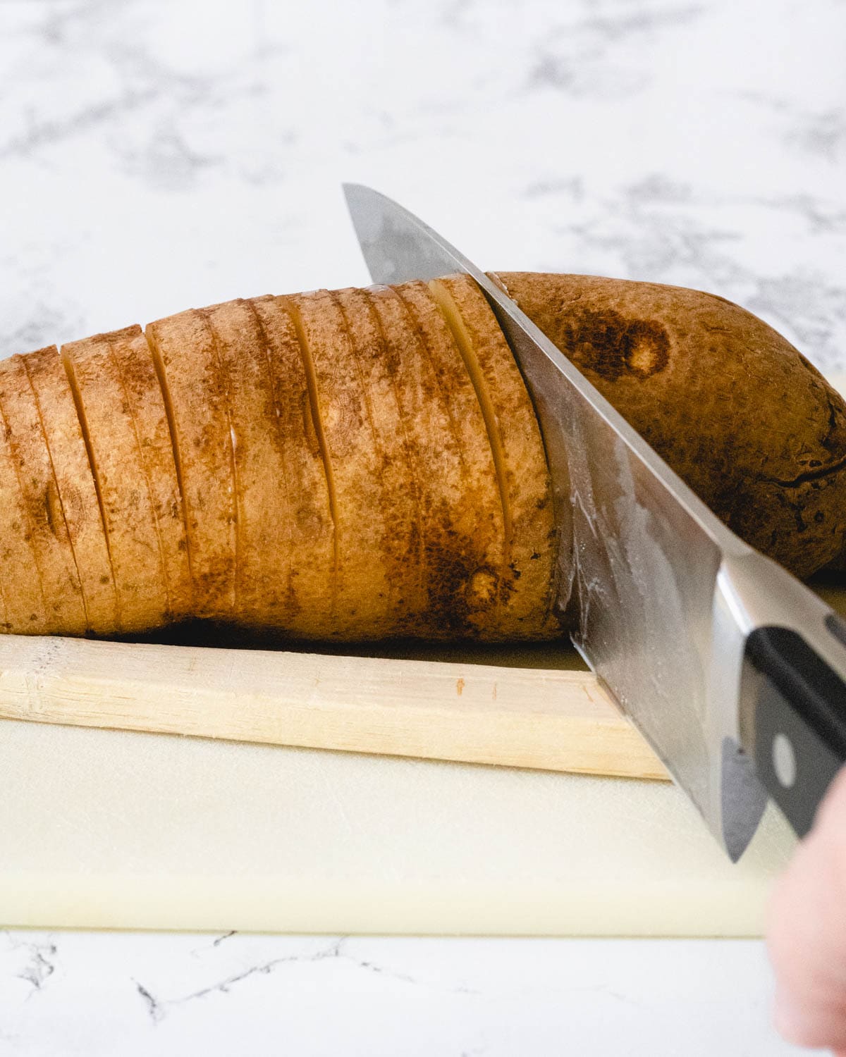 Slicing a potato in ¼-thick slices, using a spoon to stop the knife from cutting all the way through.