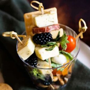 Cheese, blackberries, tomatoes, and salami skewered on fancy toothpicks and stacked in a cup.