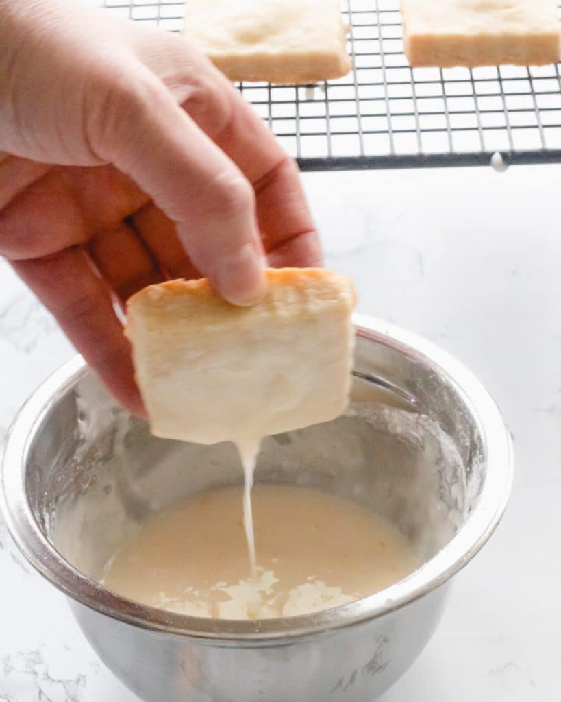 Dipping shortbread cookie into glaze.