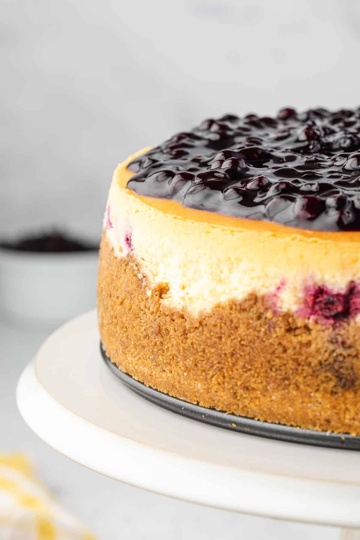Close up showing half of huckleberry cheesecake from the side, on a cake stand.