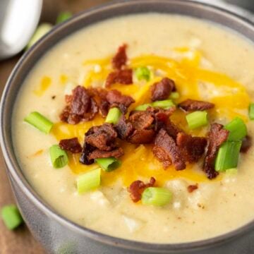 Bowl of potato soup topped with cheese, bacon, and green onions.