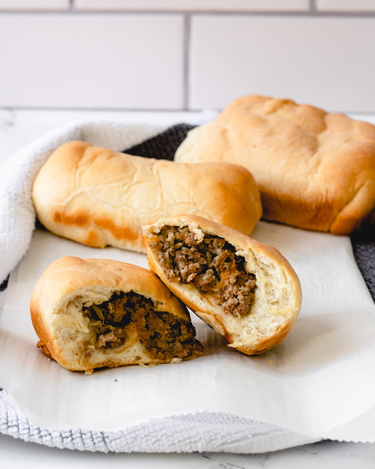 Three Runzas (bierocks) on parchment paper, one of them is cut in half and shingled.