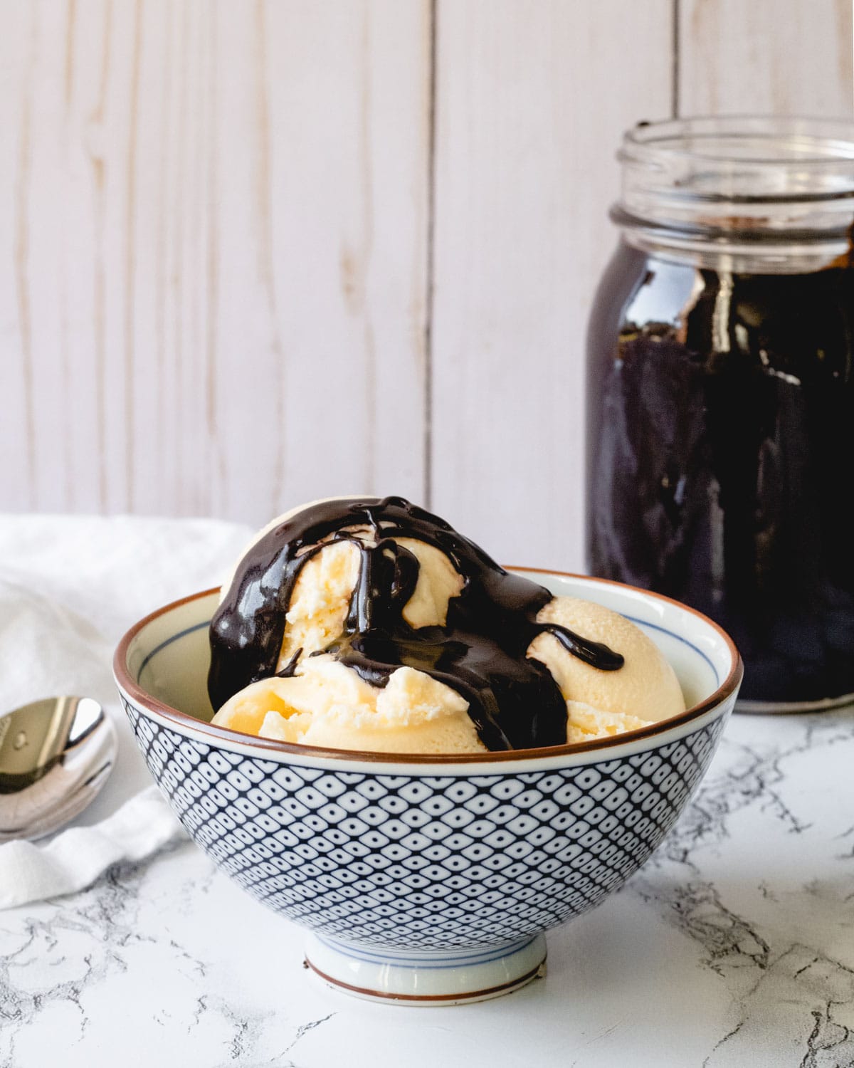 Bowl of ice cream with hot fudge, and a mason jar with hot fudge.